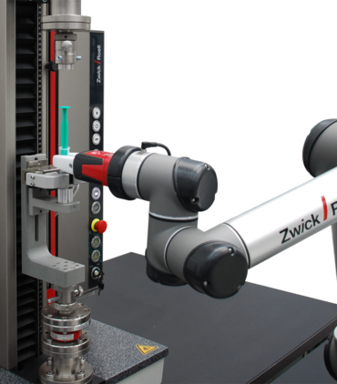 O robô de construção leve roboTest N posiciona uma seringa na máquina para ensaios e executa o ensaio de forma automatizada